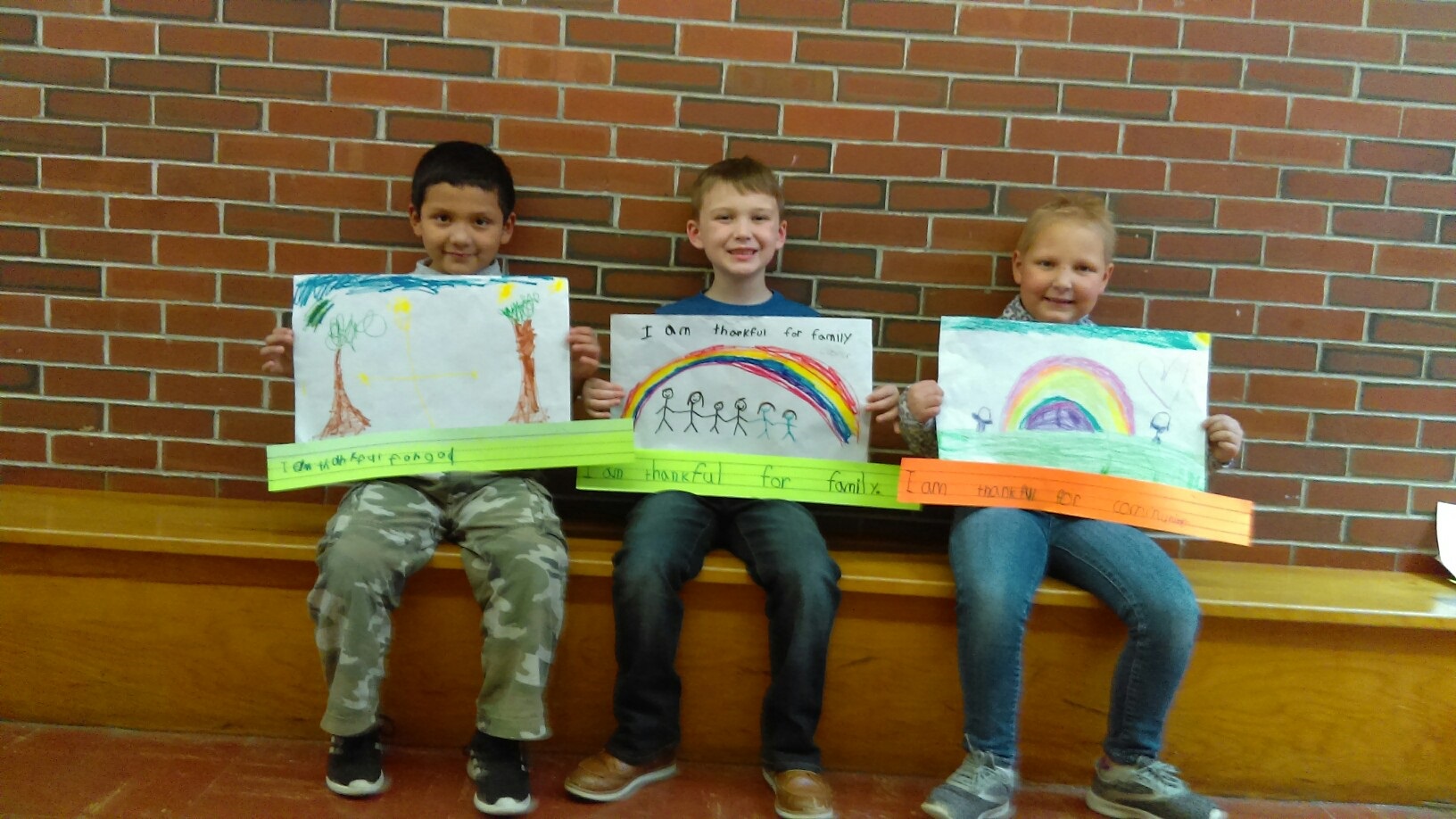 1st grade students holding drawing they made and captioned with "I am thankful for ..." sentences. 